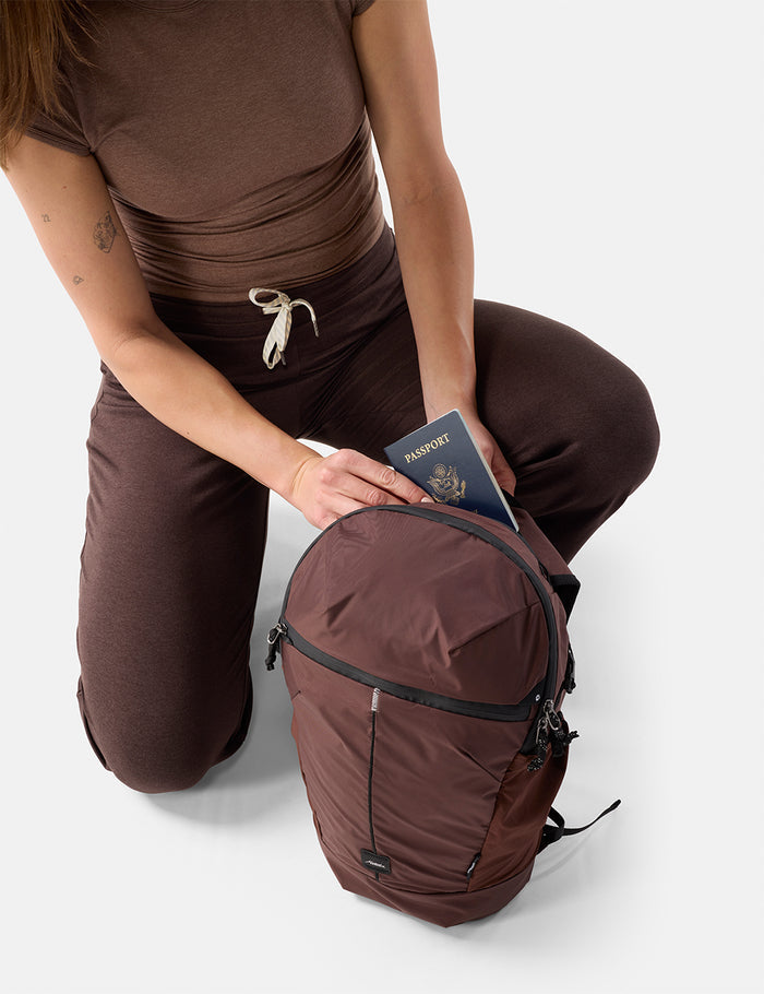 Person in brown outfit with a garnet backpack and passport on a white background