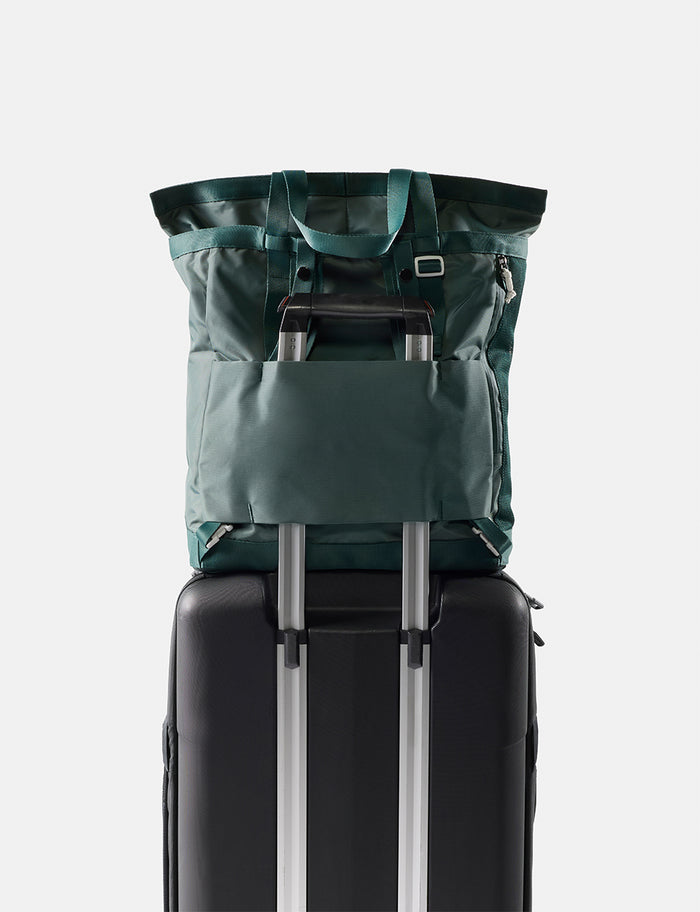 Green tote pack on top of a black suitcase with a white background
