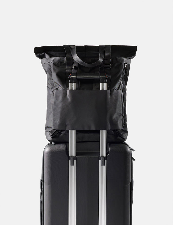 Black tote pack on top of a suitcase with a white background