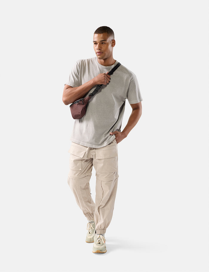 Man wearing a light gray t-shirt, beige pants, and white sneakers, holding a garnet sling on a white background