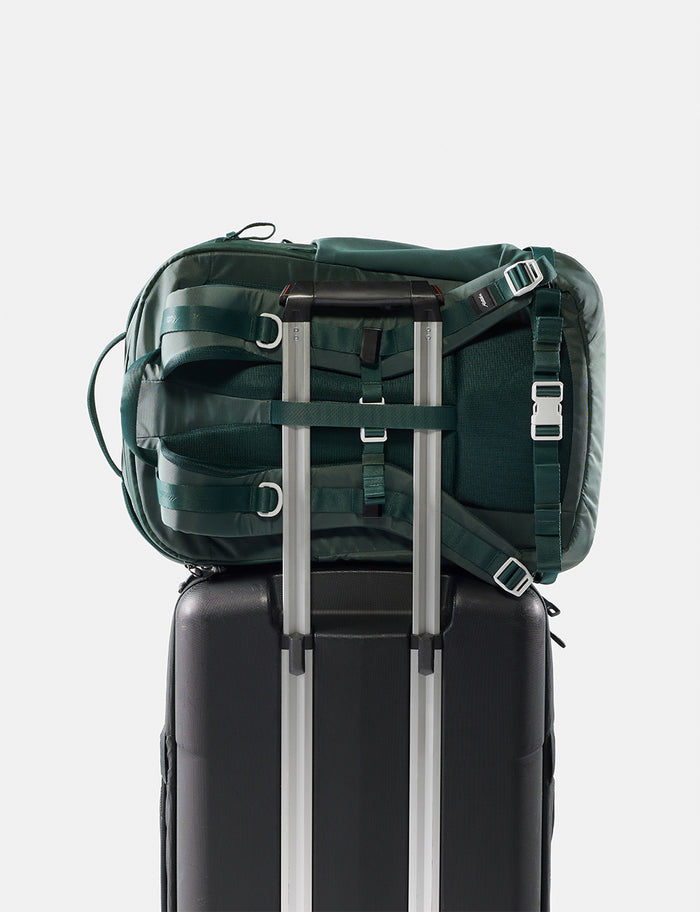 Green backpack on top of a black suitcase with silver handles on a white background