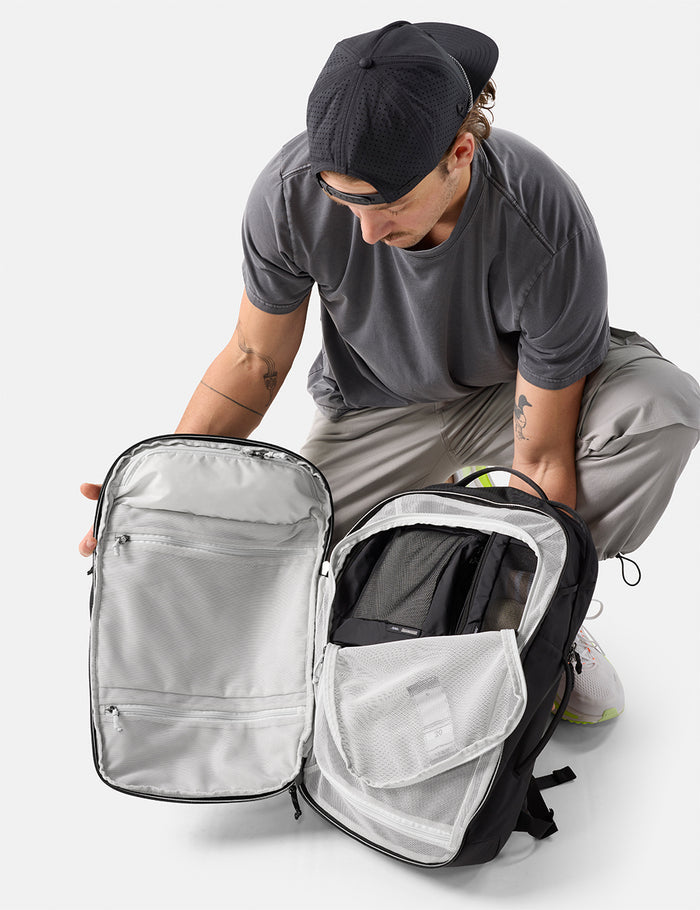Person opening a black and gray backpack on a white background