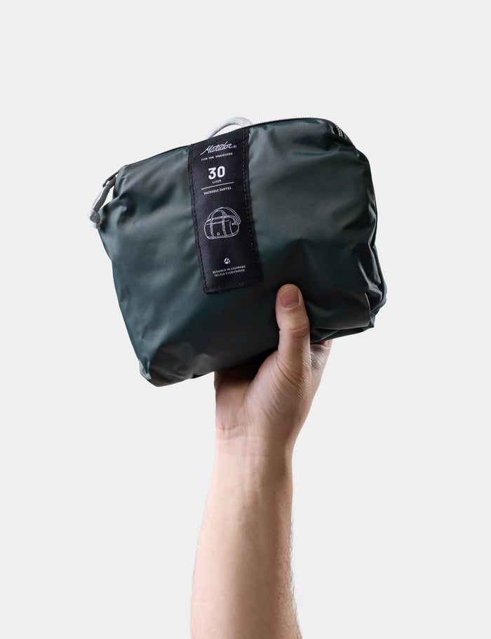 Hand holding a juniper compression bag with a visible brand label on a light gray background