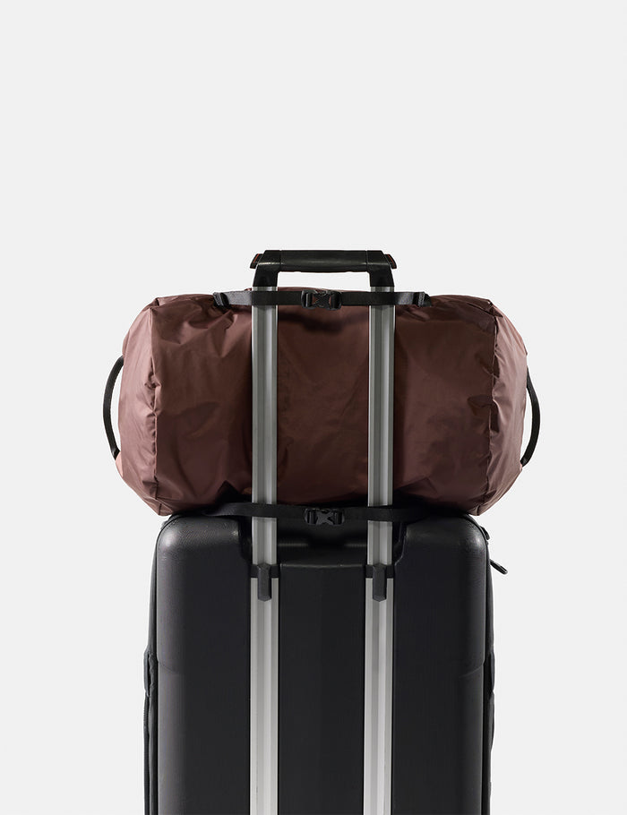 garnet duffel bag secured to a black suitcase with straps on a light gray background