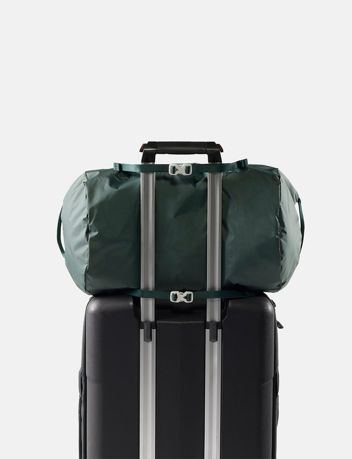 Green duffel bag tied to a black suitcase on a light gray background
