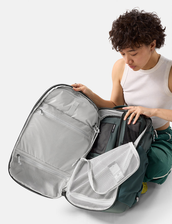 Person organizing a green backpack with multiple compartments on a white background