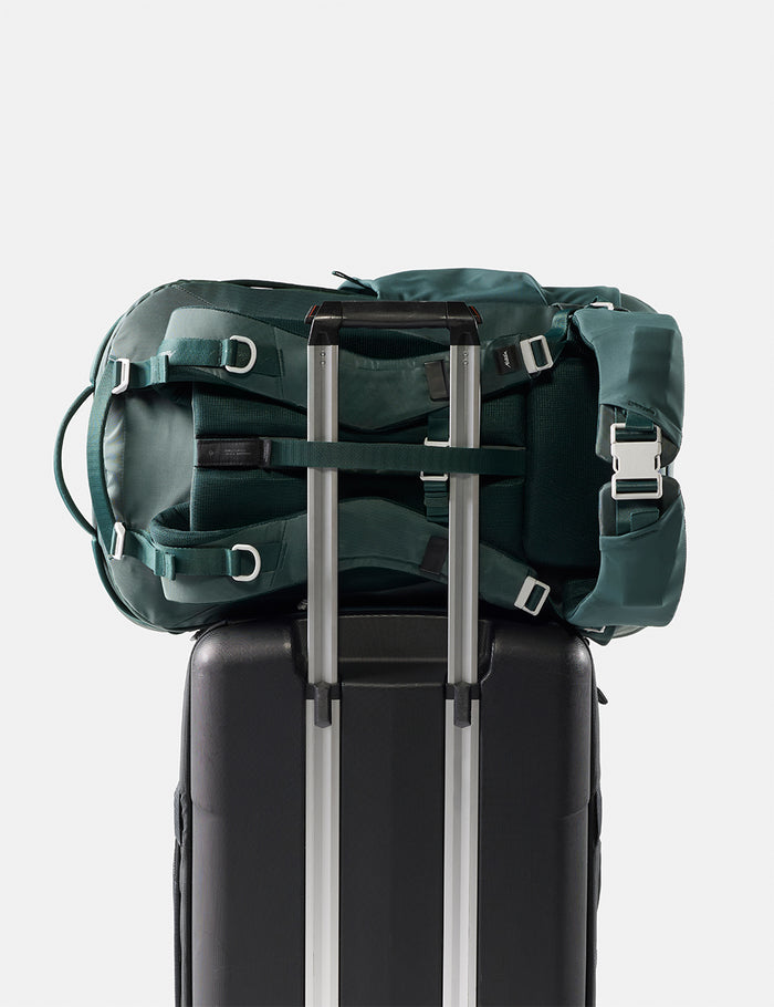 Green backpack on top of a black suitcase with a white background