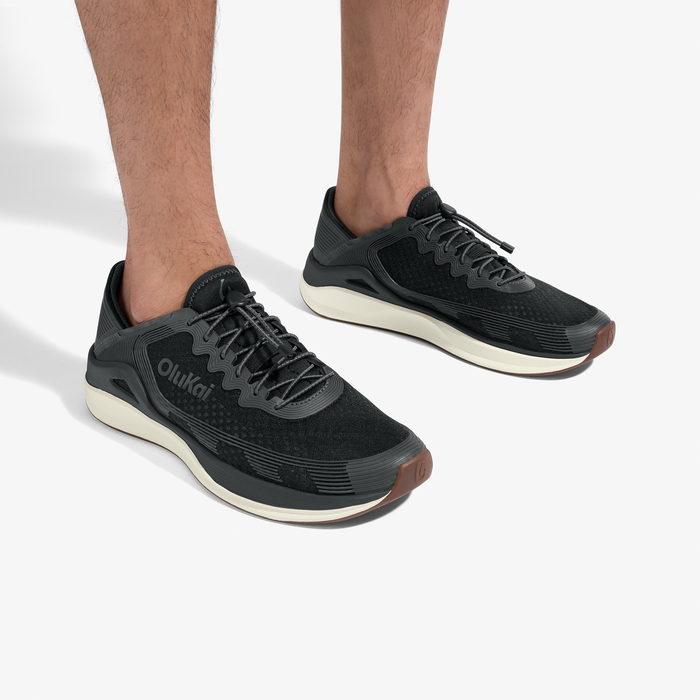 Black lace-up running shoes with cream soles and brown heel accents, worn on feet.