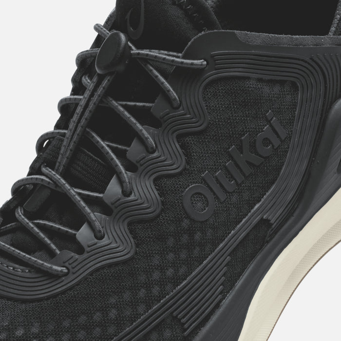 Black athletic shoe with mesh and synthetic upper, dark laces, ridged sole detail, and white midsole accent.