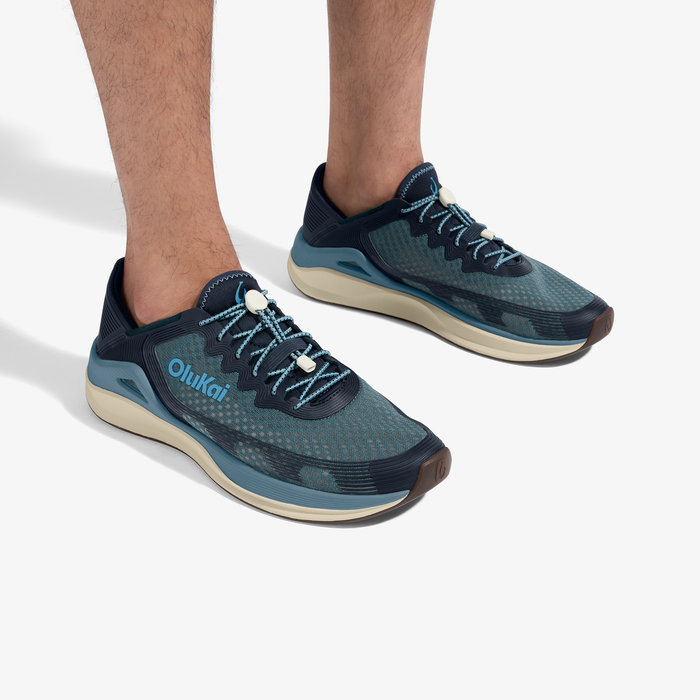Pair of dark blue and teal running shoes with cream-colored soles and light blue laces worn on male feet.