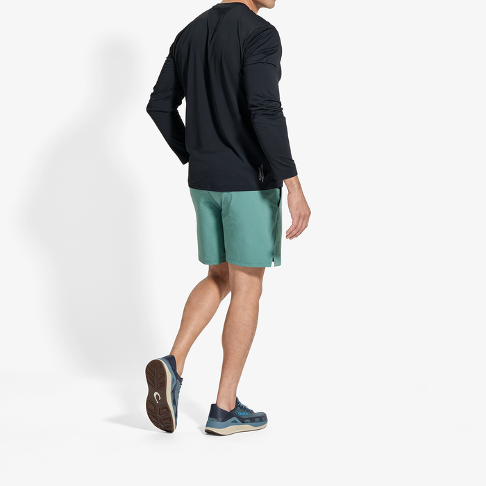 Man wearing black long-sleeve shirt and teal shorts with dark athletic shoes, shown from behind.