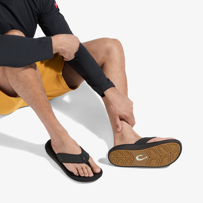 Man wearing black long-sleeve rashguard, yellow swim shorts, and black flip-flops with tan sole.