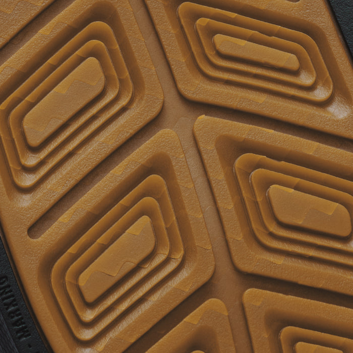 Tan rubber sole with geometric waffle tread pattern and dark material visible at edge.