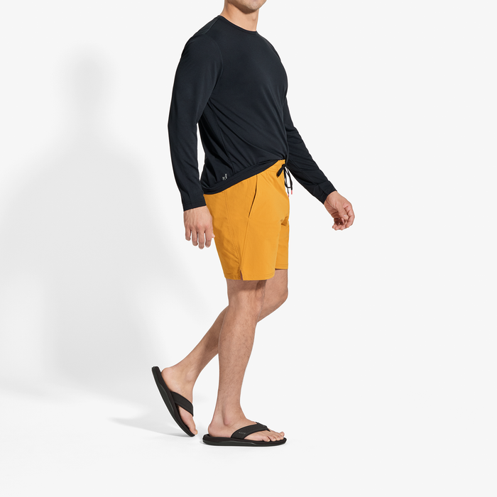 Man wearing black long-sleeve rash guard and yellow swim shorts with black sandals.