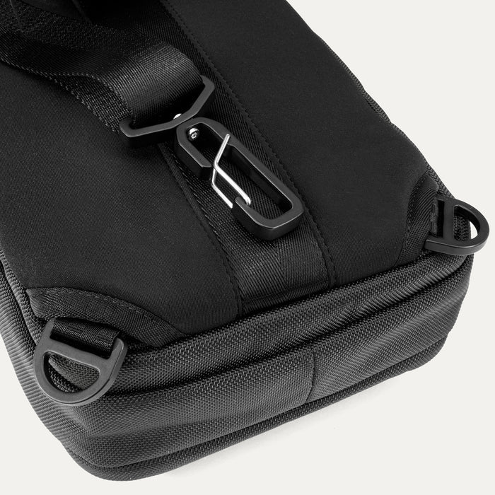 Close-up rear view of Travelpro Altitude Crossbody 6L in Black, showing D-rings and aluminum carabiner on back panel.