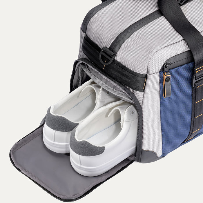 Travelpro Altitude Day-to-Day Duffel in Stellar Navy/Grey, with shoe compartment open and holding white sneakers.