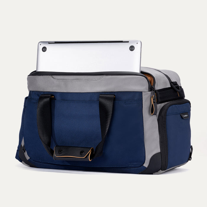 Rear angled view of the Travelpro Altitude Day-to-Day Duffel in Stellar Navy/Grey, showing laptop partially stored in padded sleeve.