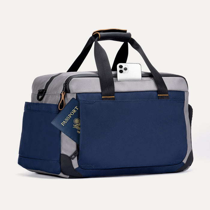 Rear angled view of the Travelpro Altitude Day-to-Day Duffel in Stellar Navy/Grey, with passport and phone in rear pocket.