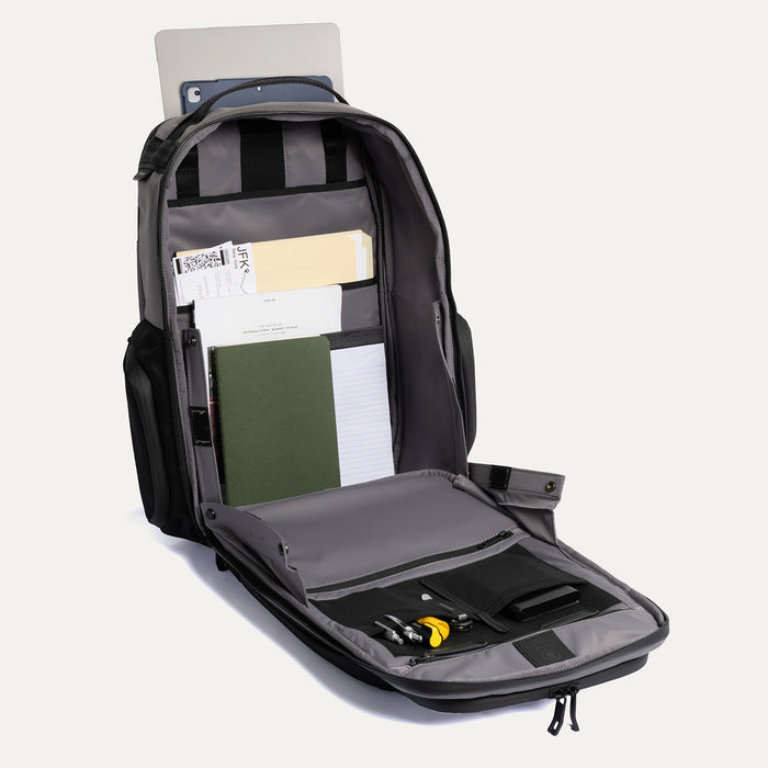 Open view of the Travelpro Altitude Large Expandable Laptop Backpack in Falcon Grey, showing organized compartments with a laptop, folders, and accessories on a light gray background.