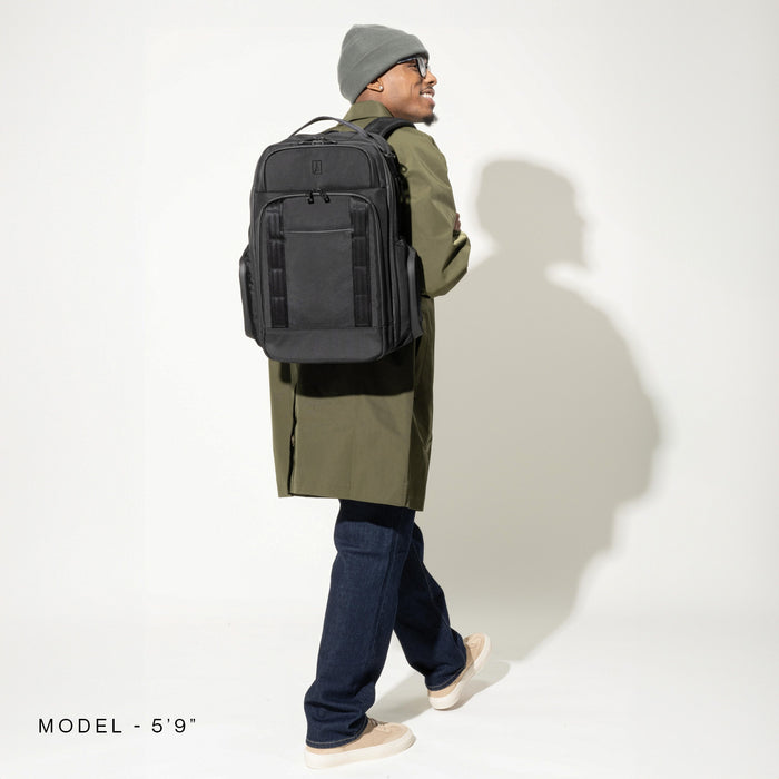 Lifestyle view of a man wearing the Travelpro Altitude Large Expandable Laptop Backpack in Black, walking in profile against a white background. Model height 5'9".