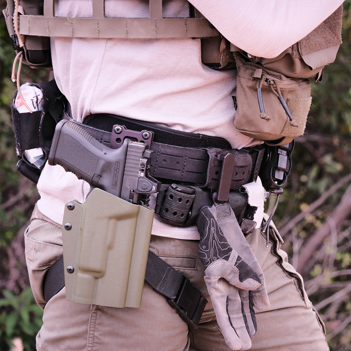 Side view of a Person wearing a black Kore Essentials laser cut B1 battle belt and other tactical gear with a rifle and backpack in an outdoor setting