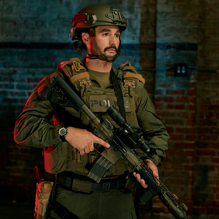 A police officer in tactical gear stands in a warehouse holding a rifle and wearing a black laser cut Kore Essentials Molle Battle Belt