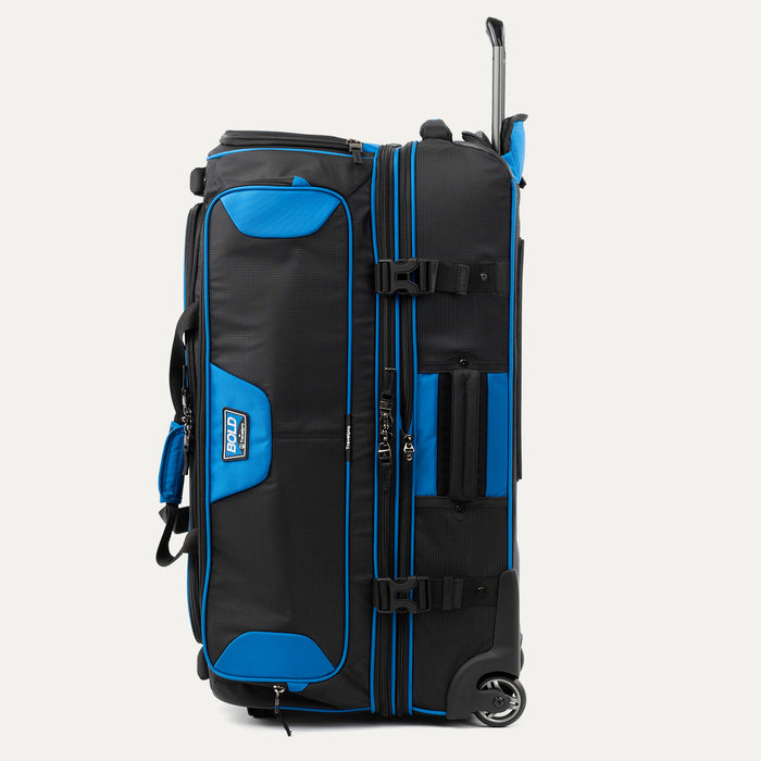 side view of the blue black bold by travelpro large check-in drop-bottom rolling duffel bag standing vertically, showing its sturdy side carry handle, exterior compression straps with buckles, and the extended telescoping handle.