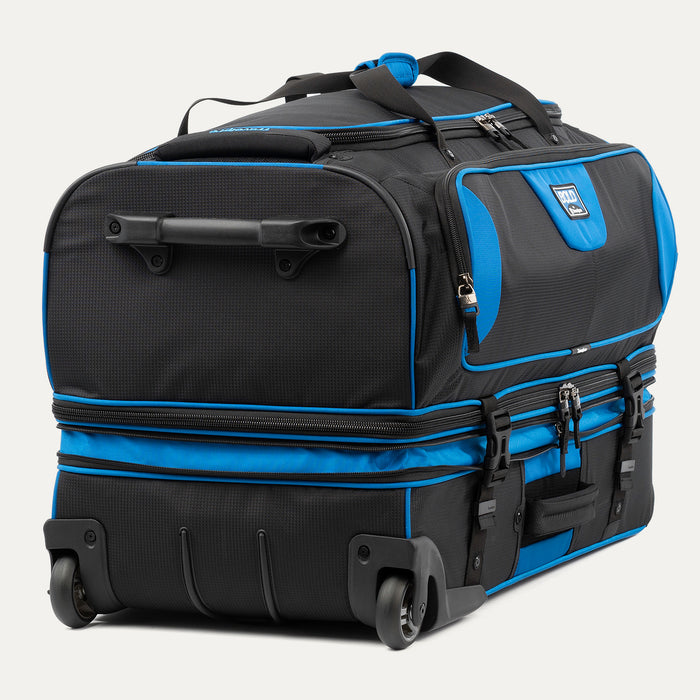 low-angle rear view of the blue black bold by travelpro large check-in drop-bottom rolling duffel bag resting horizontally, showcasing its two high-performance wheels, heavy-duty bottom skid guards, and the retracted telescoping handle base.