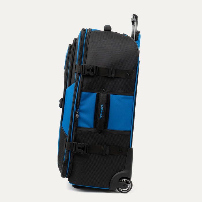 side view of the blue black bold by travelpro large check-in expandable rollaboard suitcase standing vertically, showing its durable blue fabric accent panels, side carry handle, exterior compression straps with buckles, and the extended telescoping handle.