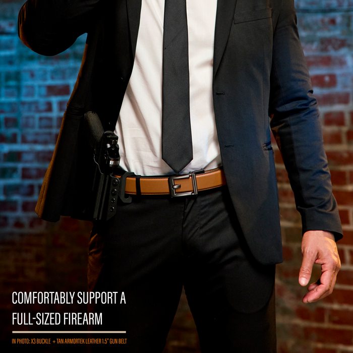 A person stands wearing a black suit and a Kore Essentials tan 1.5" Armortek Leather EDC gun belt. Text on the image reads "comfortable support a full-sized firearm." Beneath that text reads "in photo: x3 buckle + tan armortek leather 1.5" gun belt."