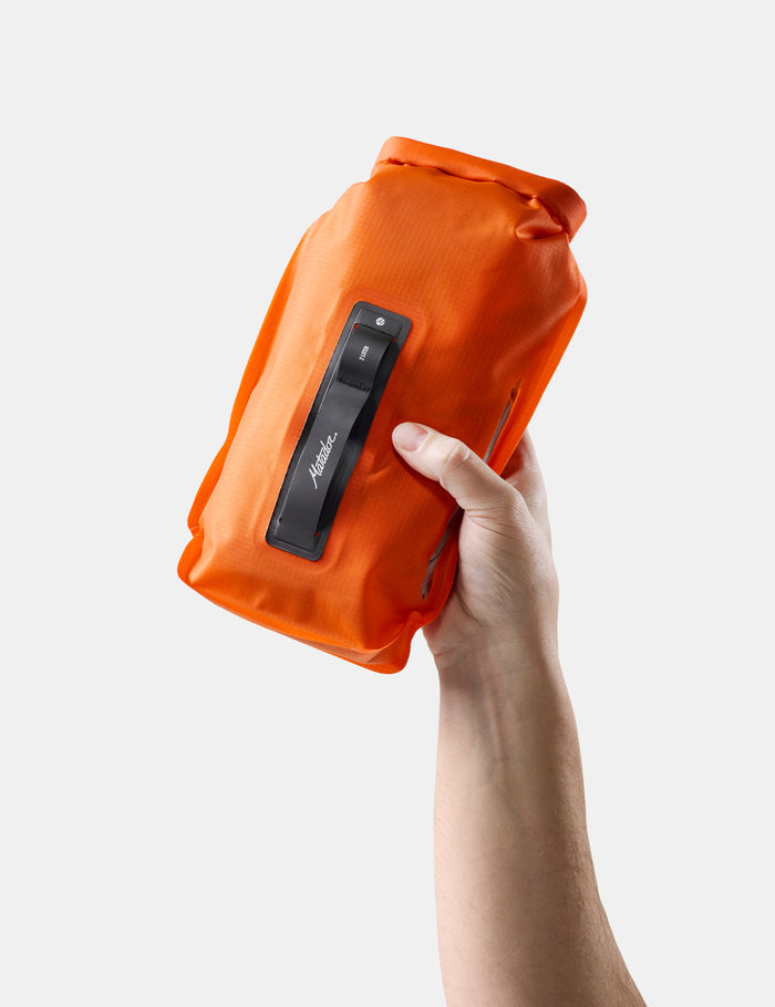 Orange dry bag held by a hand on a white background