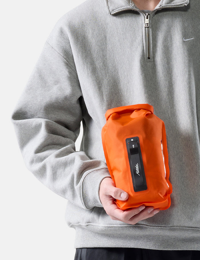 Person holding an orange dry bag against a white background