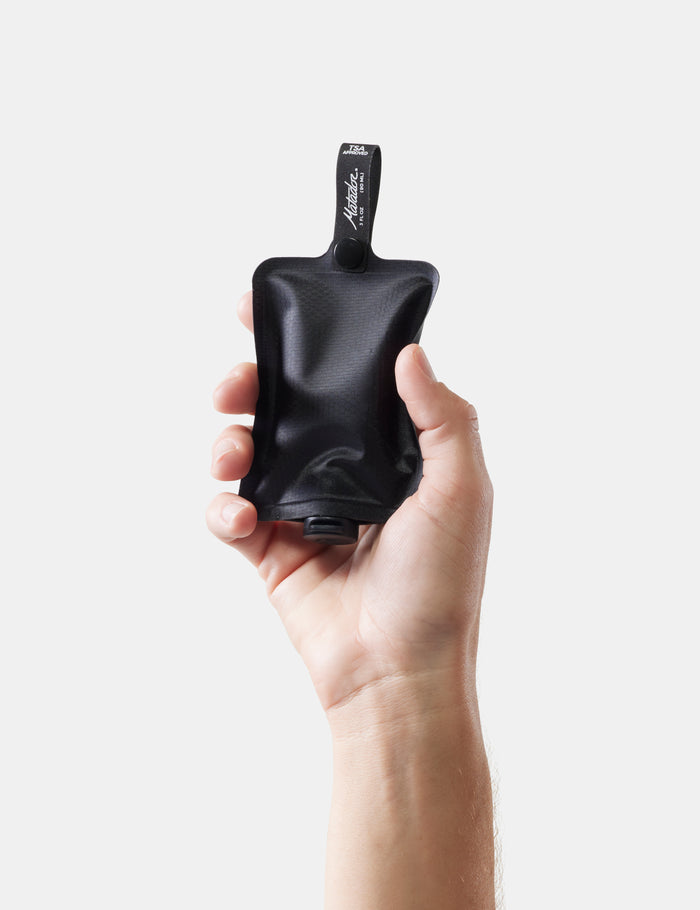 Hand holding a black toiletry bottle on a white background