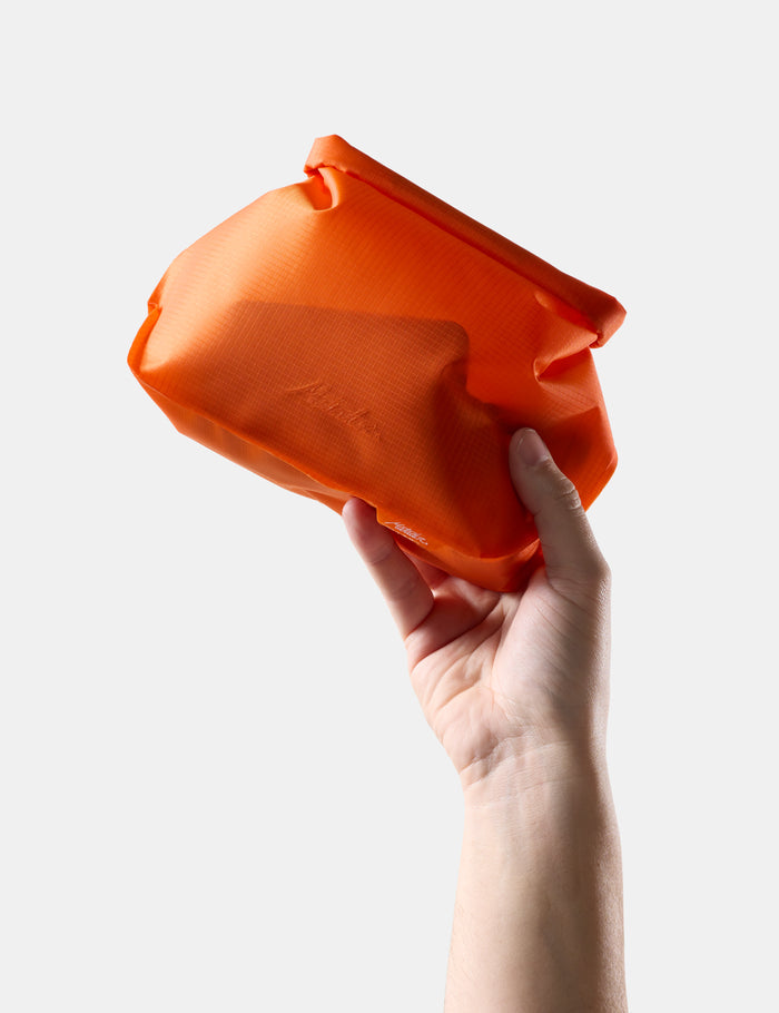 Hand holding an Orange toiletry bag against a white background