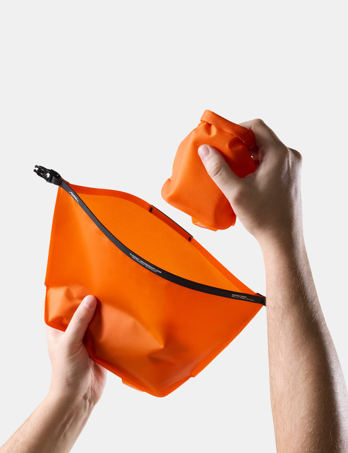 Orange toiletry bag with a hand holding an orange soap bar case against a white background