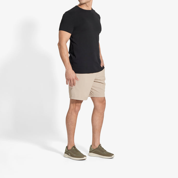 Man wearing black short-sleeve t-shirt, beige shorts, and olive lace-up sneakers.