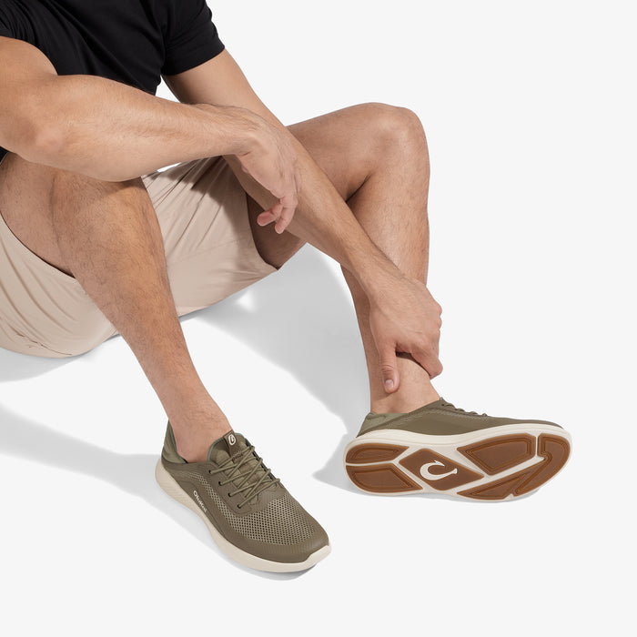 Man wearing olive and cream sneaker with visible sole pattern, paired with beige shorts and black shirt.
