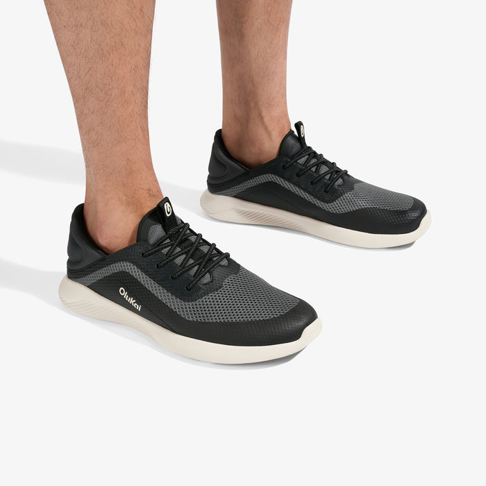 Black and gray mesh sneakers with cream-colored soles, shown on a person's feet from the side and back angles.