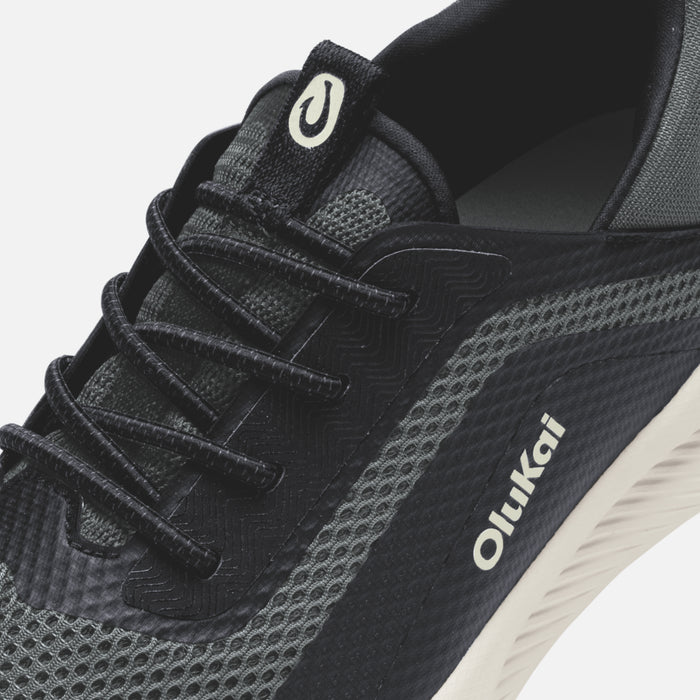 Black and gray athletic shoe with lace-up closure, curved heel tab, and white sole with Olukai branding.
