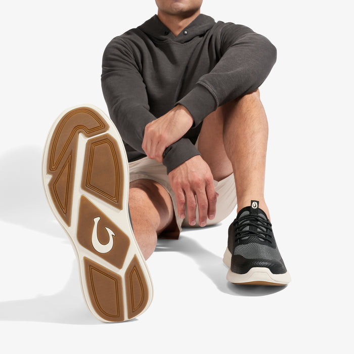 Man wearing dark gray hoodie and shorts with black and white sneaker, showing tan and white sole detail.