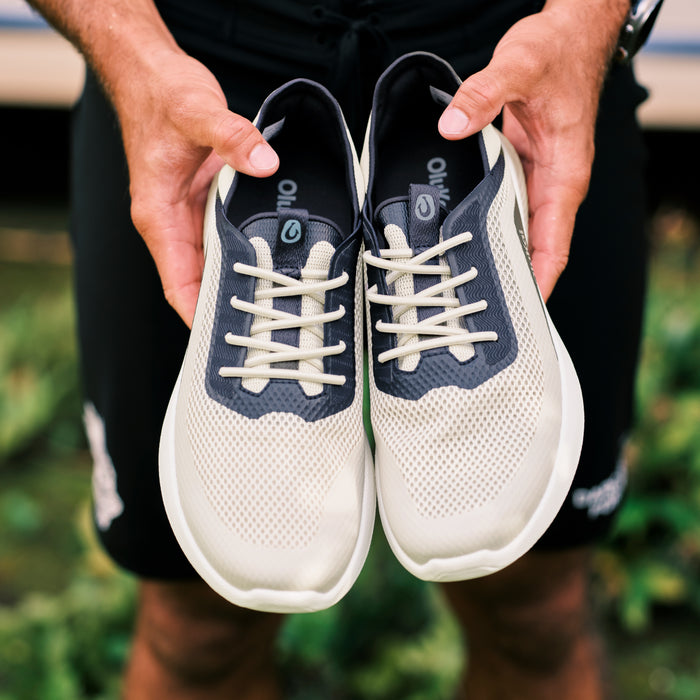 White and navy lace-up sneakers with cream-colored laces held in person's hands.