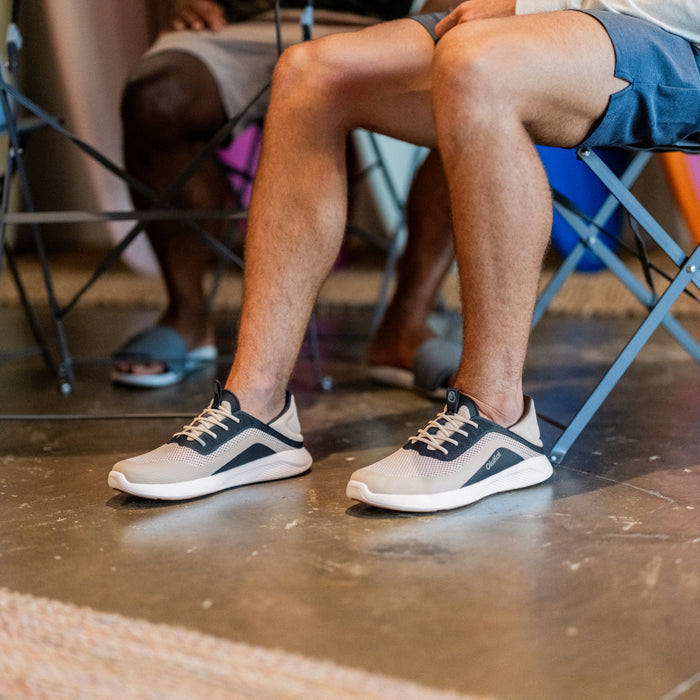 Person wearing Kialoa Tapa sneakers in trench blue with white and navy colorway while seated outdoors.