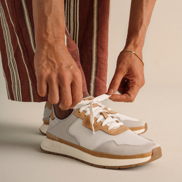 White and tan lace-up sneaker with mesh panels and cream sole, styled with striped burgundy shirt.