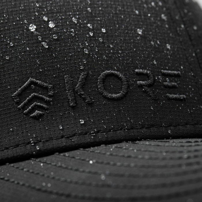 Closeup Shot of Black Kore Essentials Water Repellent Crew Hat with Grey Kore Logo on Front of Hat Showcasing Water Repellent Feature