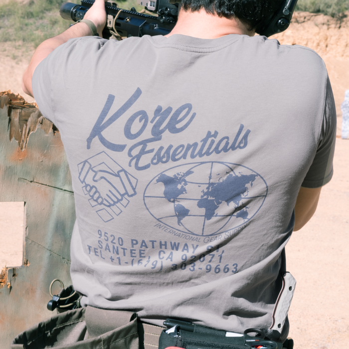Person wearing a gray t-shirt with 'Kore Essentials' branding outdoors.