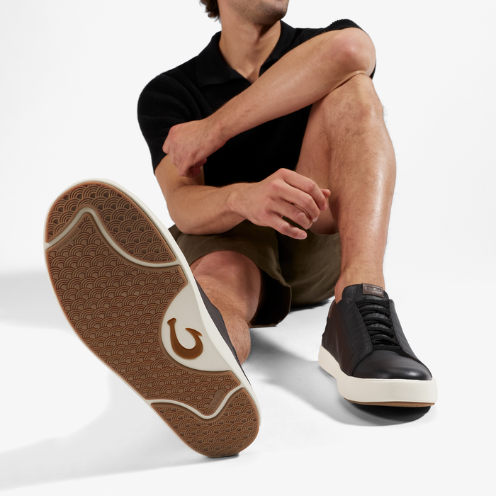 Man wearing black short-sleeve shirt and olive shorts with black and cream sneaker featuring tan patterned sole.