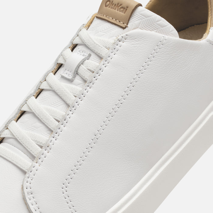 White leather sneaker with tan heel tab and white laces showing stitched detail and side stripe.