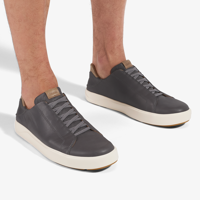 Man wearing dark gray lace-up sneakers with cream sole and tan heel collar detail.