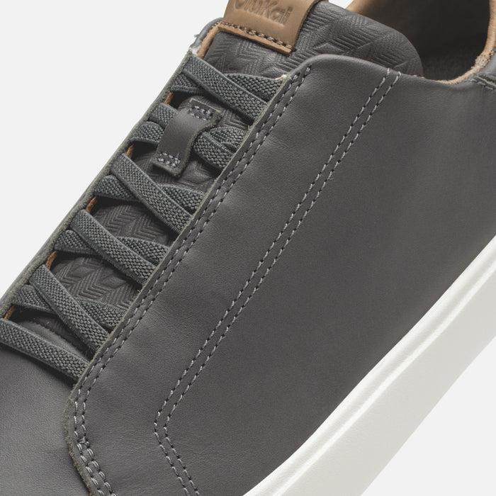 Gray leather sneaker with tan heel tab, textured laces, and white sole, shown in close-up detail.