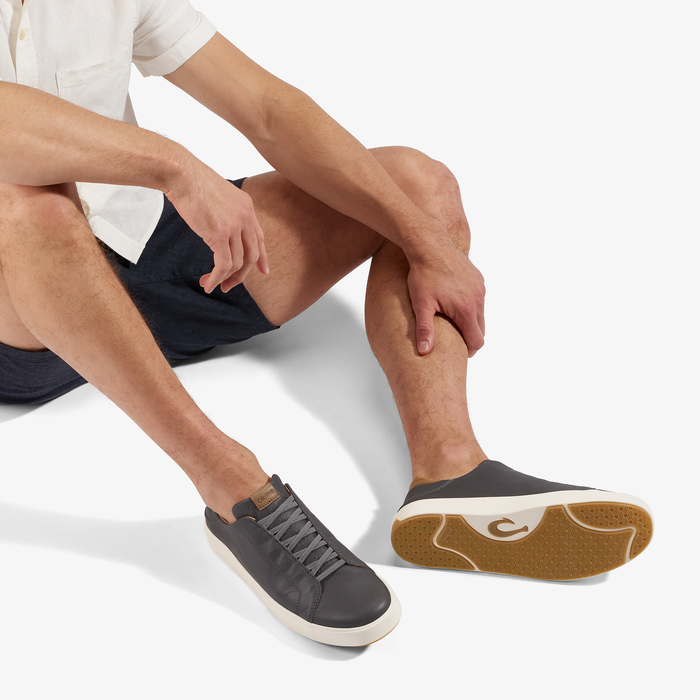 Man wearing white shirt and dark shorts seated, displaying black sneaker with white sole and tan gum outsole.